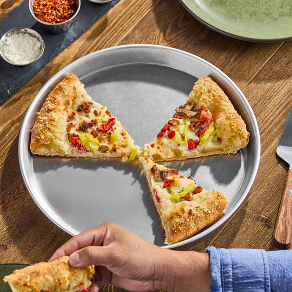 A round, silver aluminum deep dish pizza pan holding three slices of pizza.