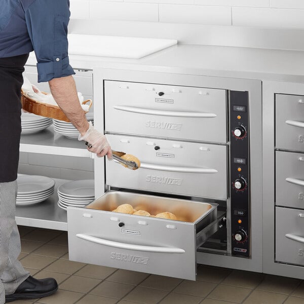 A man using a ServIt triple built-in drawer warmer to put food in a metal container.