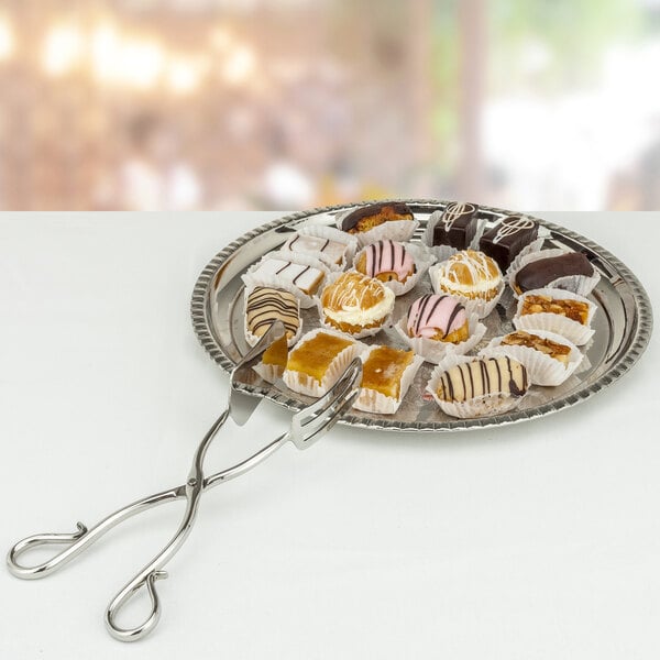 A silver tongs picking up a pastry from a plate of pastries.