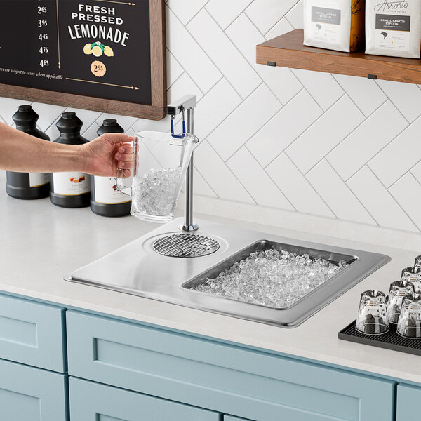 A person using a Delfield drop-in water station to fill a pitcher with ice.
