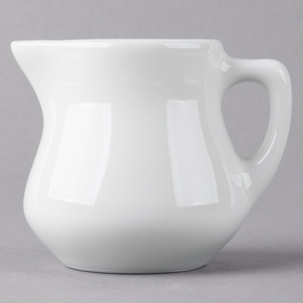 A white Tuxton porcelain creamer pitcher with a handle.