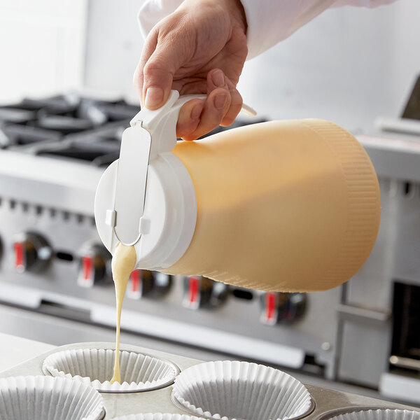 A person pouring batter from a white Vollrath Dripcut server into cupcake cases.