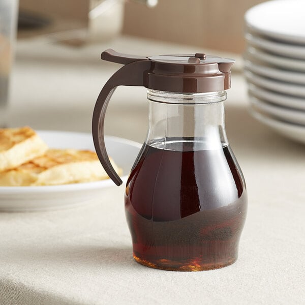 A clear polycarbonate teardrop syrup server with a brown lid on a table in a breakfast diner.