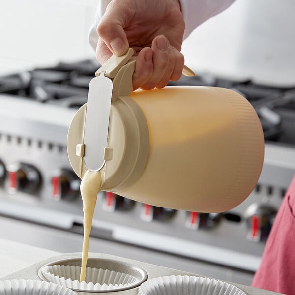 A person pouring batter from a Vollrath Dripcut server into a cupcake tin.