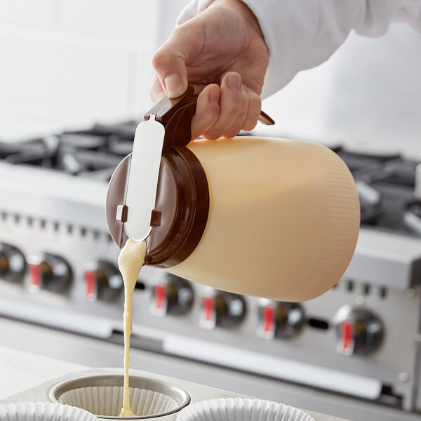 A person pouring cream from a Vollrath Dripcut server into a cupcake tin.