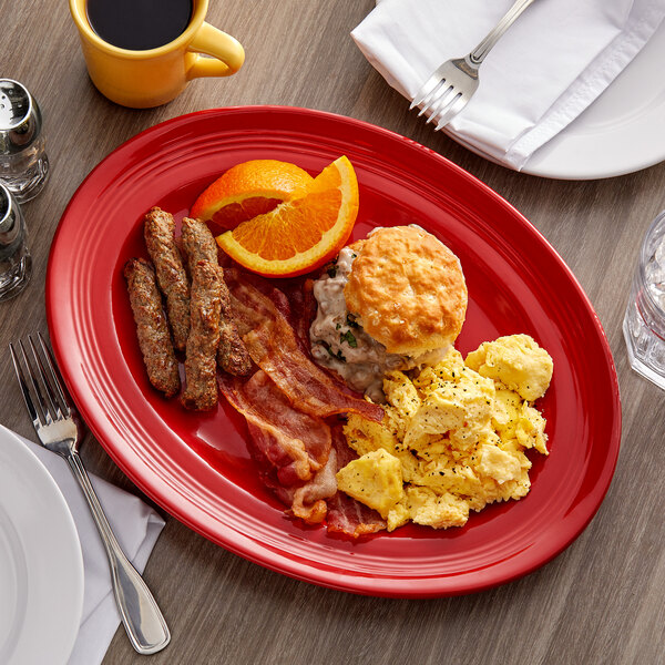 A Tuxton cayenne oval china platter with breakfast food on it, including a sliced orange.