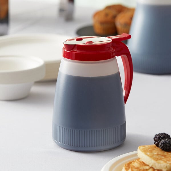 A Vollrath Dripcut Polyethylene server with a red top on a table filled with liquid.