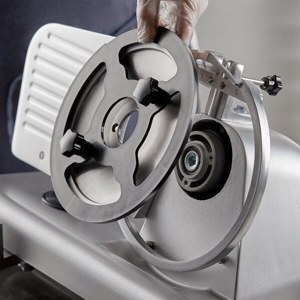 A person's gloved hand using the Avantco blade removal tool to remove a meat slicer blade.
