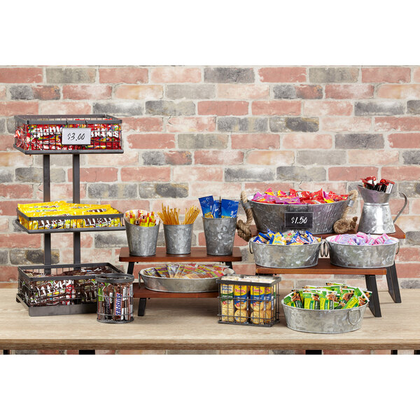 An oval galvanized tray with handles holding a variety of snacks and candy on an outdoor table.