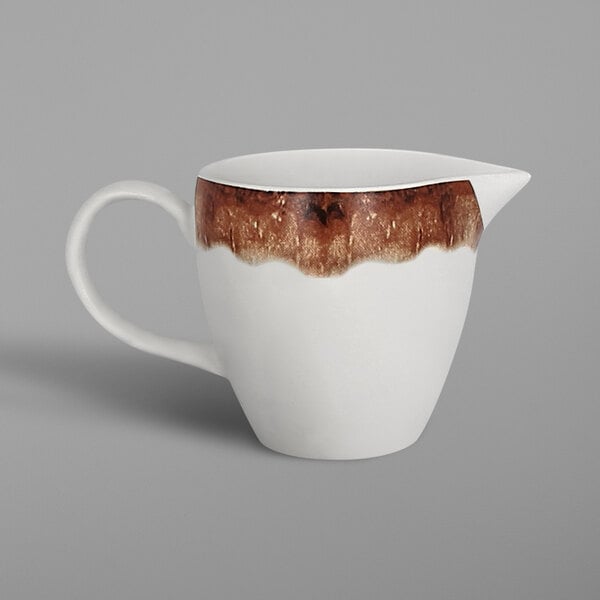 A white porcelain creamer with a brown and white design on the rim.