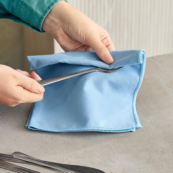 A person using a pair of scissors to cut a Carlisle blue microfiber cloth.
