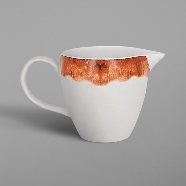 A white porcelain creamer with a brown rim and orange and brown accents.