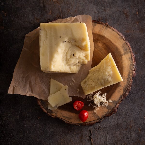 A block of Centro Form Pecorino cheese with black summer truffles on a wooden plate.