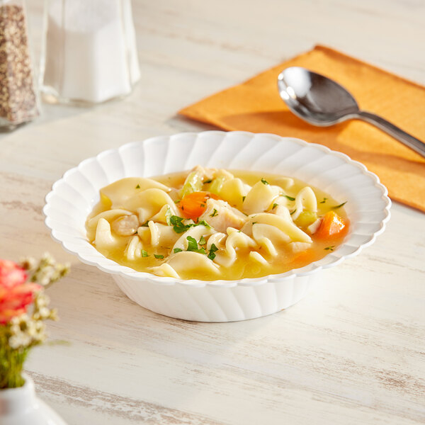 A white WNA Comet disposable plastic bowl filled with noodle soup with vegetables and a spoon.