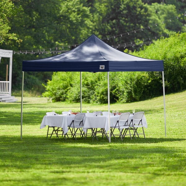 A table with a white tablecloth set up under a navy Backyard Pro Courtyard canopy on grass.