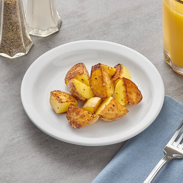 A plate of fried potatoes and a fork on a Acopa stoneware plate with a glass of juice.