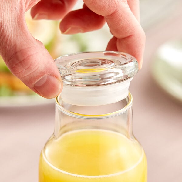 A hand pouring orange juice into a Libbey glass bottle on a table.