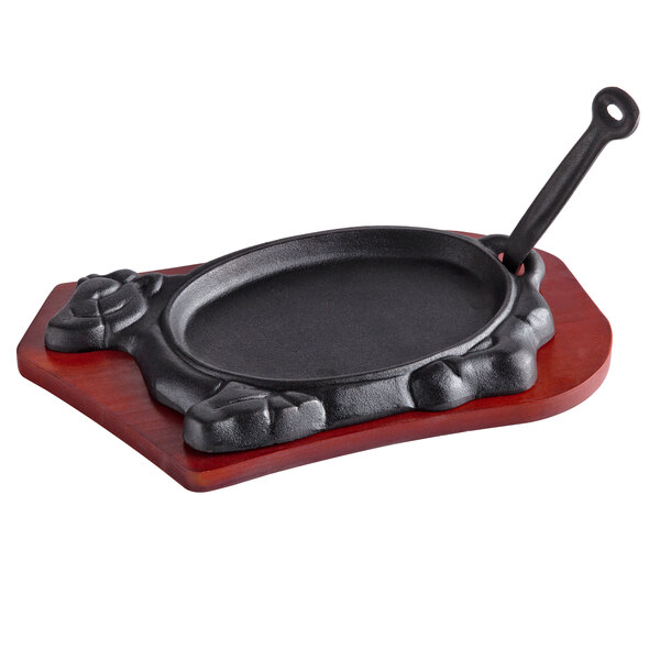 A cast iron Thunder Group oval fajita skillet on a wood underliner.