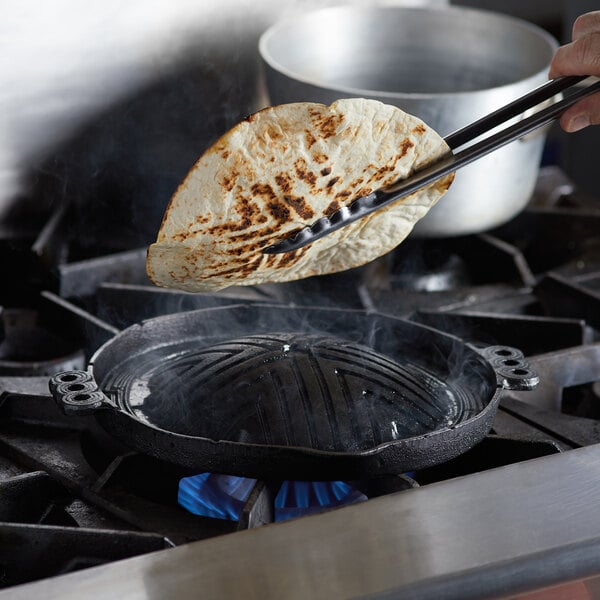 Man holding grilled tortilla over cast iron barbecue plate on range