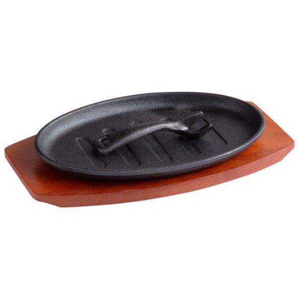 A black cast iron Thunder Group fajita skillet on a wooden stand.