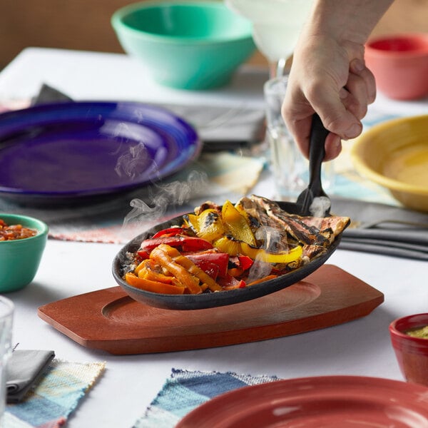 A person holding a Thunder Group oval cast iron skillet over a plate of sizzling food.