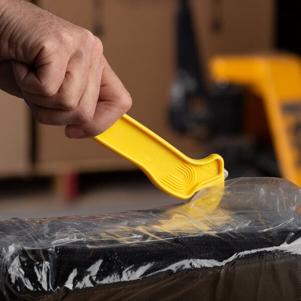 A hand using a Pacific Handy Cutter DFCNSFY to remove a plastic bag.