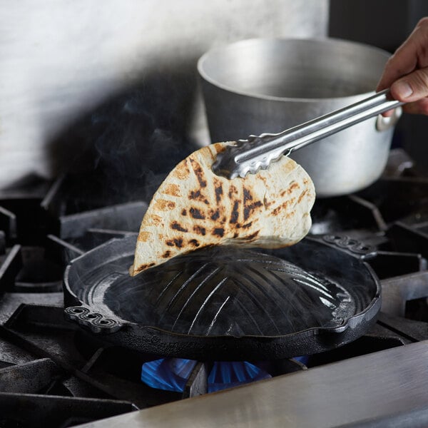 A person using tongs to cook a tortilla on a Thunder Group cast iron stovetop BBQ plate.