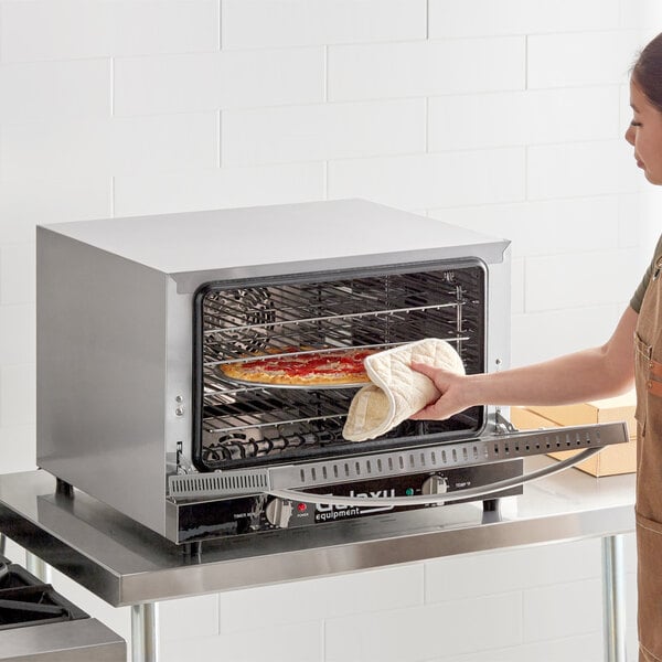 A woman using a Galaxy countertop convection oven to bake a pizza.