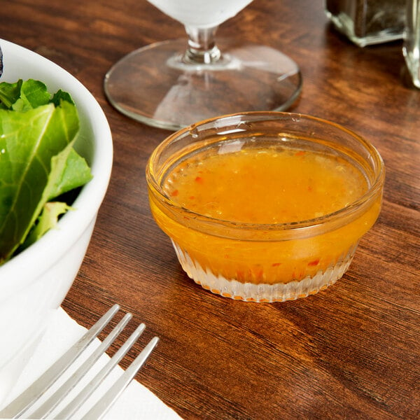 A Libbey Winchester glass filled with orange liquid on a table with a bowl of salad.