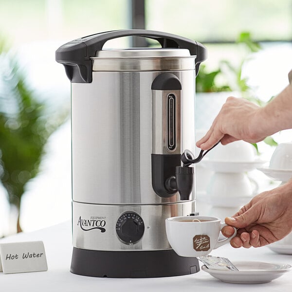 A person pouring a cup of tea from an Avantco hot water dispenser.