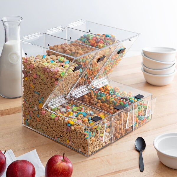 A plastic container with cereal and a red apple on a table with a white bowl.