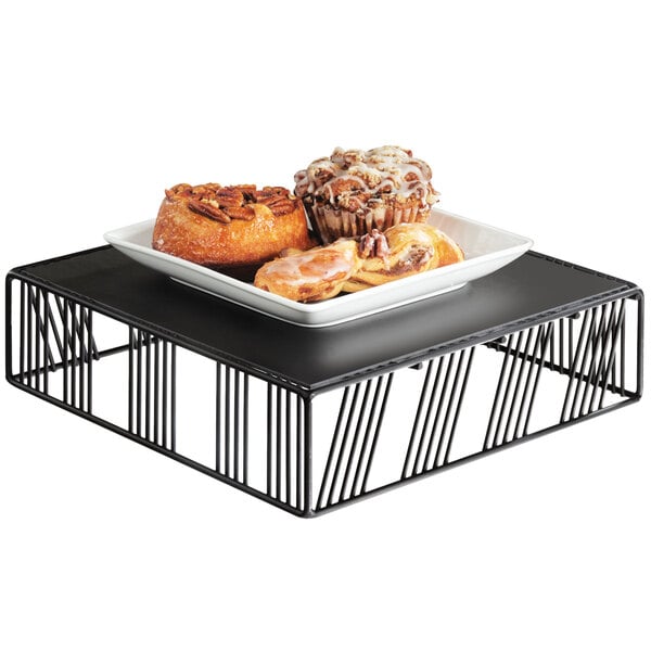 A black Cal-Mil metal riser holding a tray of pastries.