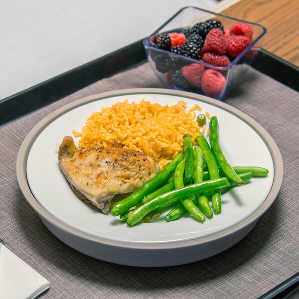 A plate of rice and chicken on a Dinex induction base plate with a bowl of fruit.