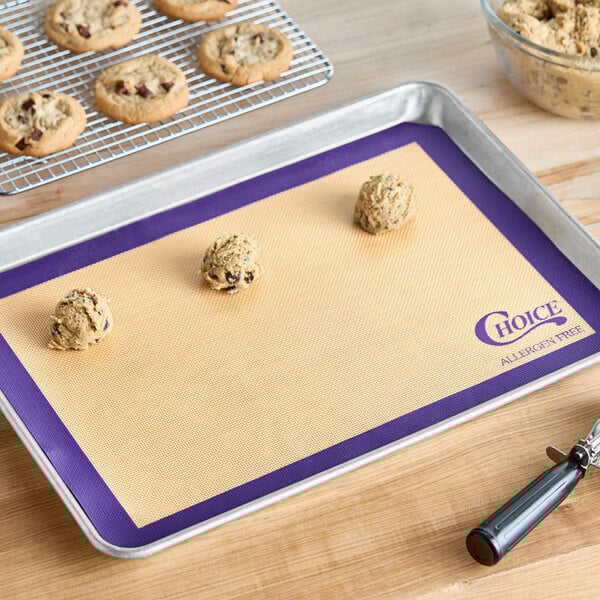 A purple silicone baking mat with cookies on a tray.