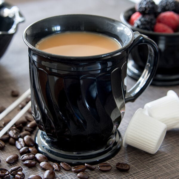 A close-up of a black Dinex Turnbury insulated mug with brown liquid and a spoon.