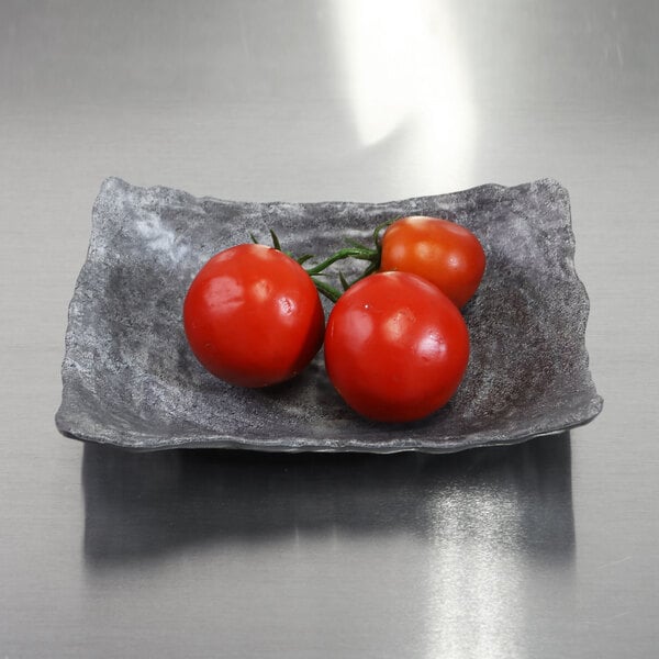 A rectangular coal colored melamine bowl filled with tomatoes on a table.