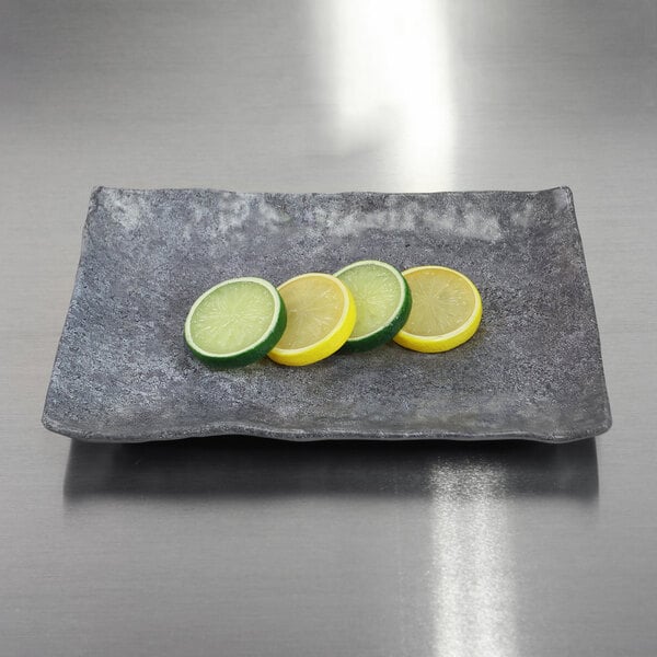An Elite Global Solutions Basalt rectangular melamine plate with slices of lemons and limes on it.