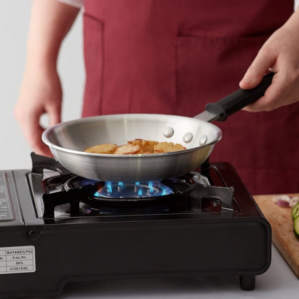 A person cooking food in a Choice aluminum fry pan on a stove.