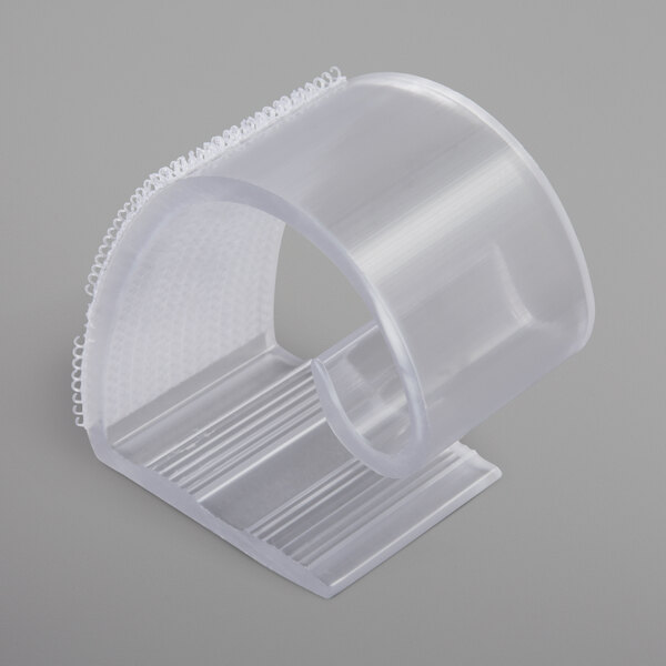 A clear plastic table skirt clip with white hook and loop attachment.