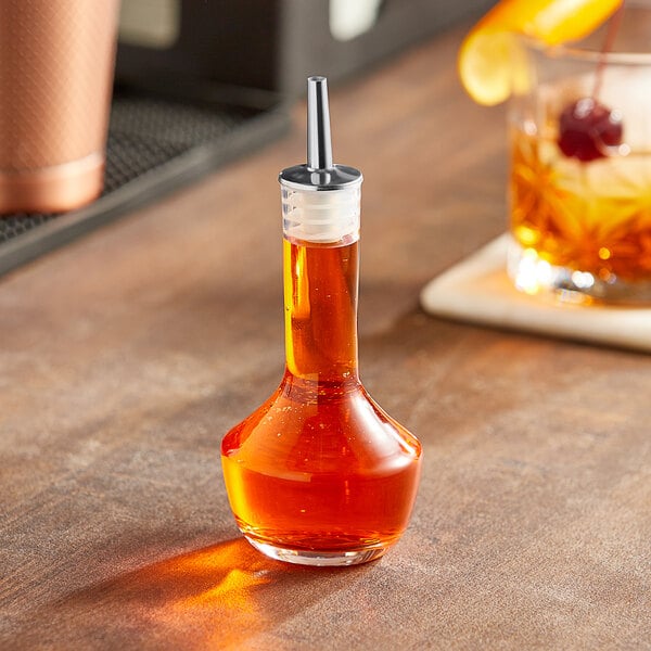 An Acopa clear glass bitters bottle with a liquid inside on a table.