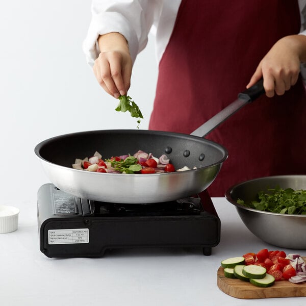 A person cooking leafy greens in a Choice aluminum non-stick fry pan.