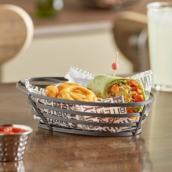 A GET metal gray oval wire basket with food and a sauce cup on a table.