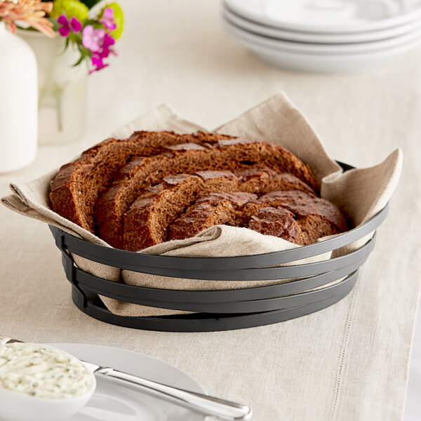 A metal gray wire basket with a loaf of bread on a table.