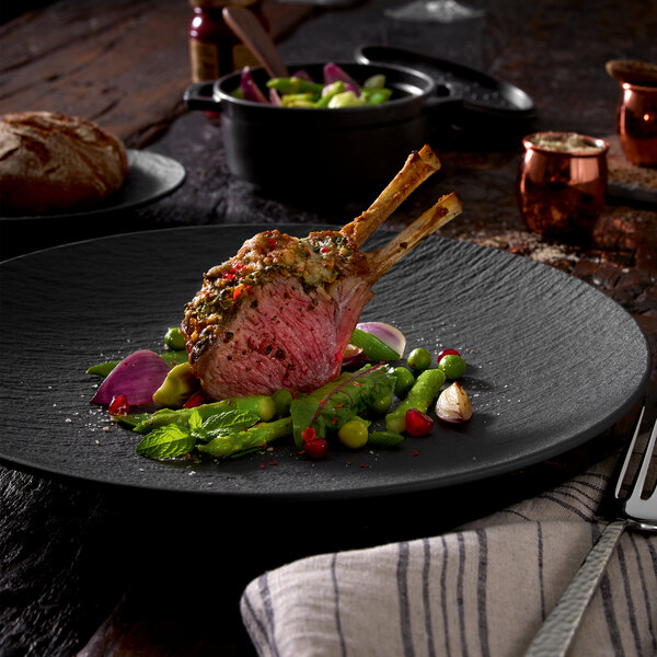 A black Villeroy & Boch porcelain plate with meat and vegetables on it.