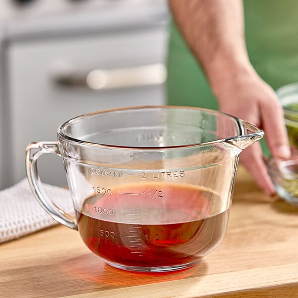 A hand using an Anchor Hocking glass measuring cup to measure brown liquid.