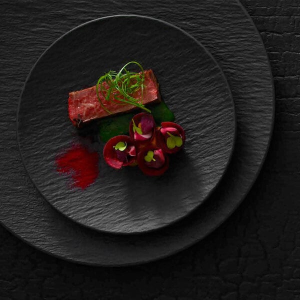 A Villeroy & Boch black shale porcelain plate with food and green sprigs.