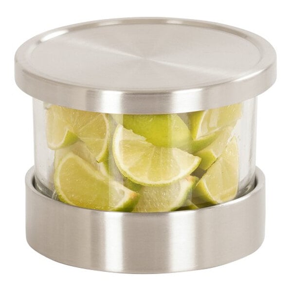 A large glass mixology jar set with stainless steel accents, filled with lime wedges.