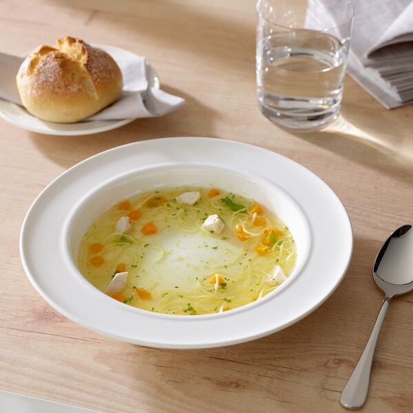 A white porcelain bowl of soup with bread on a table.