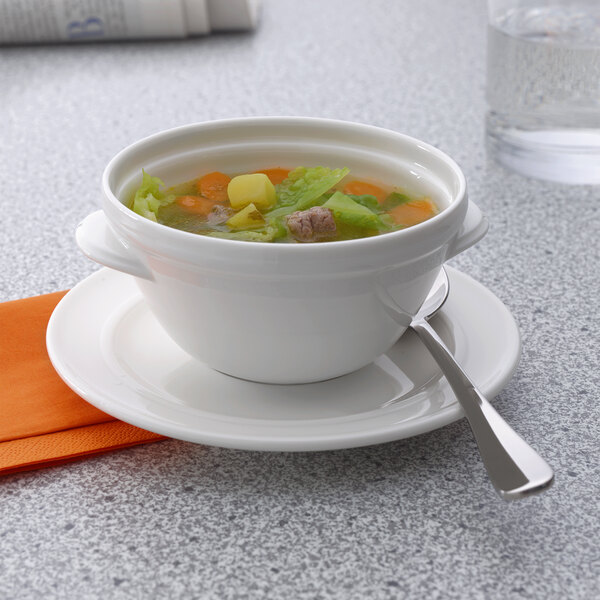 A Villeroy & Boch white porcelain bowl filled with soup on a plate with a spoon.