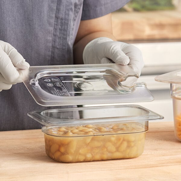 A person in gloves holding a Cambro clear plastic container of food with a lid.